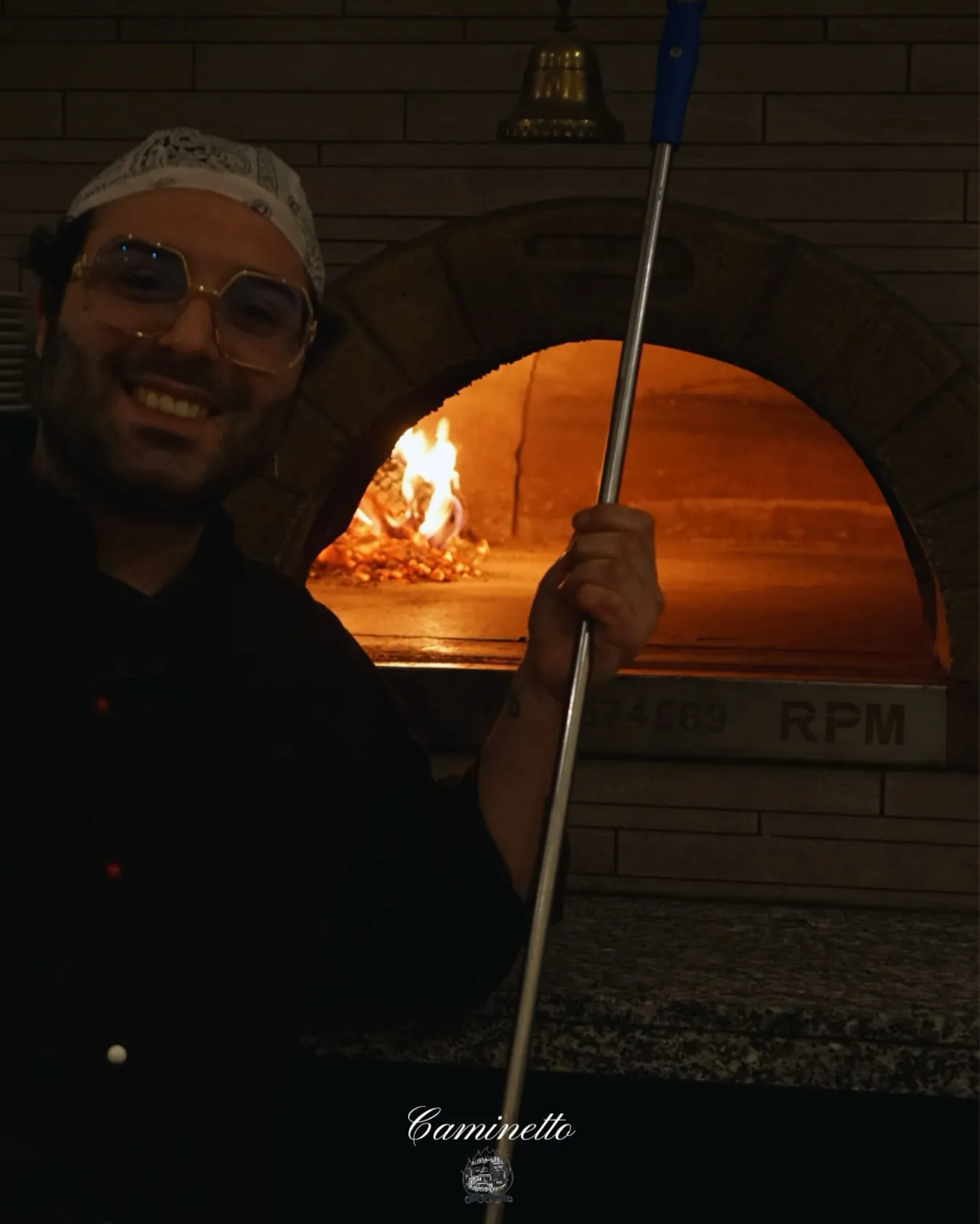 Junger Pizzaiolo lächelt am Ofen mit Feuer.