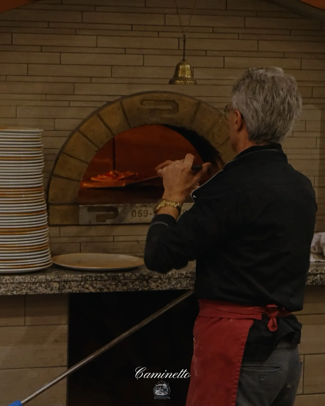 Erfahrener Pizzaiolo schiebt eine Pizza in den lodernden Holzofen.